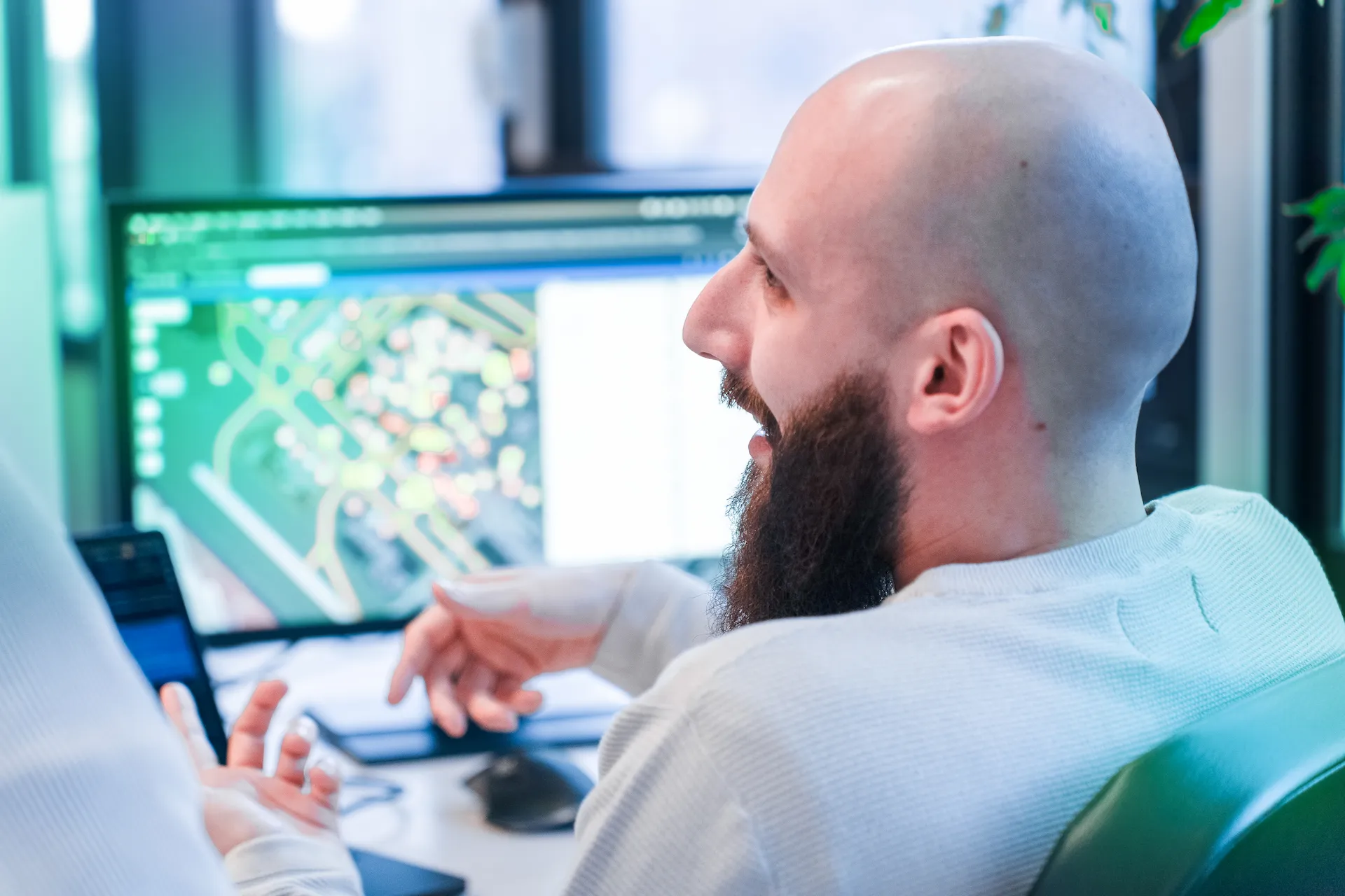 Sviluppatore di Winet che sorride mentre discute di un progetto software per Thales, con un monitor sullo sfondo che mostra un’interfaccia di mappatura.